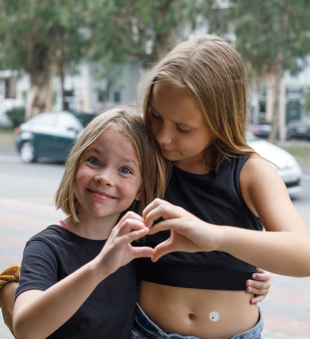 Two children making a heart shape with their hands, one wearing a sensor